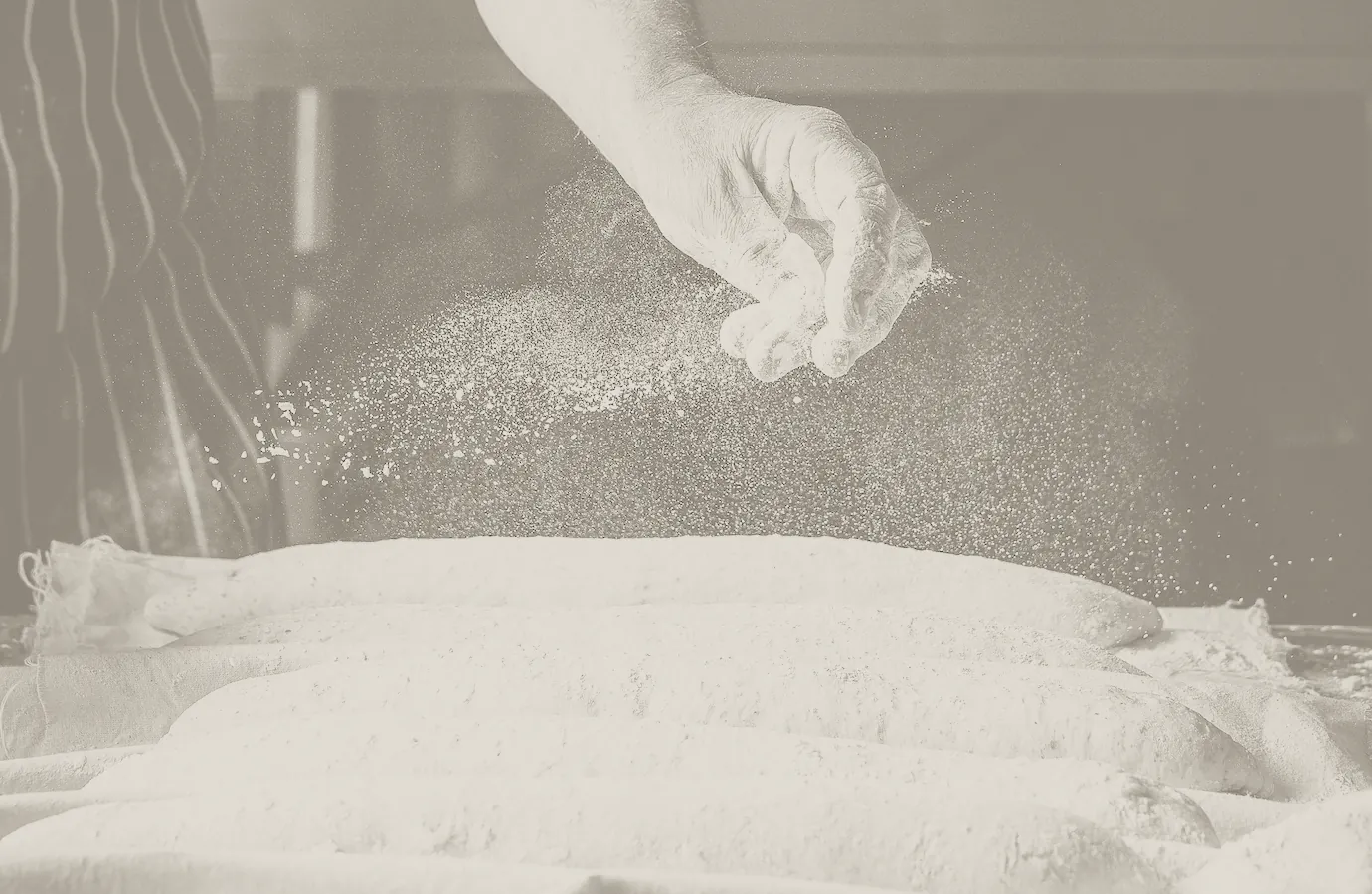A baker dusting a row of loaves with flour