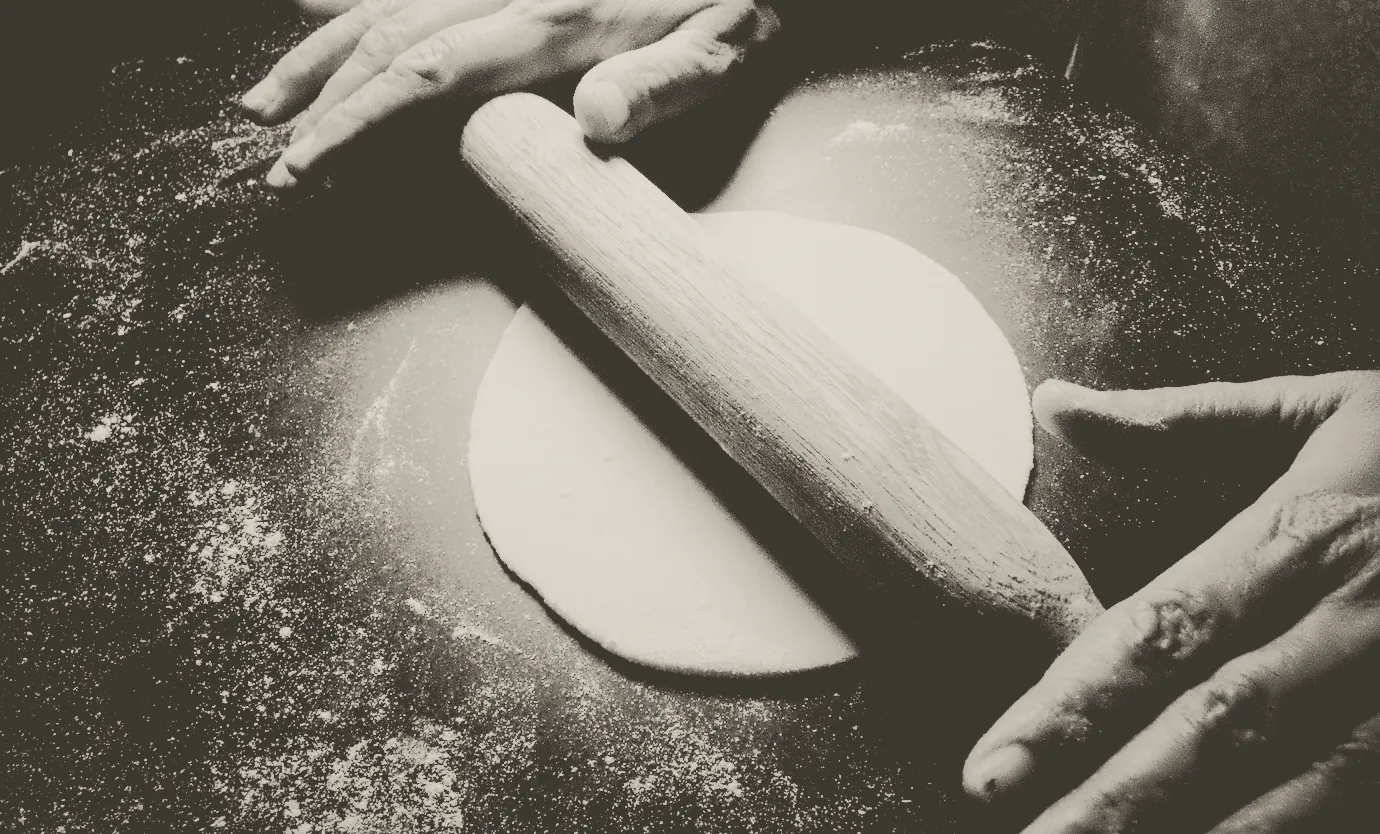 Dough rolled out with a wooden pin, flour across the bench
