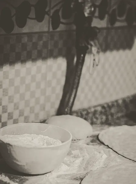 A bowl of flour and rounds of dough on the bench