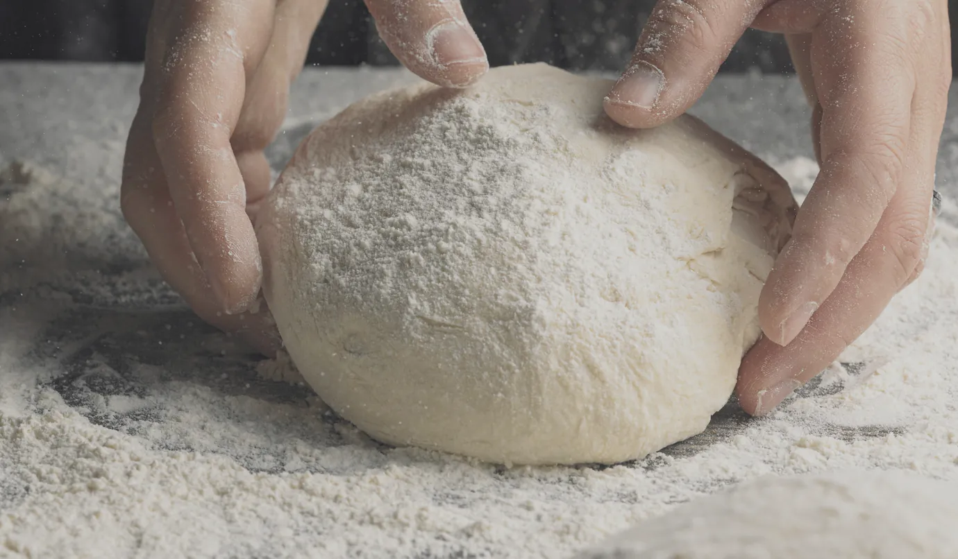 Floured hands cupping a round of dough on the bench