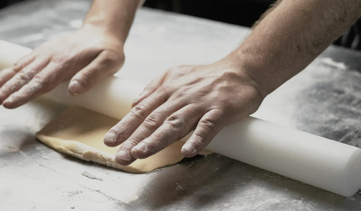 Hands rolling out dough with a long pin