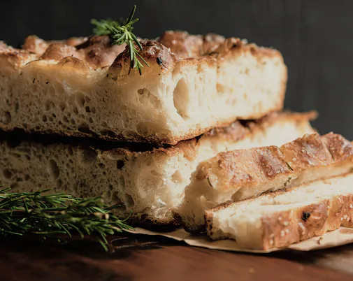 Slices of rosemary focaccia stacked on a dark board
