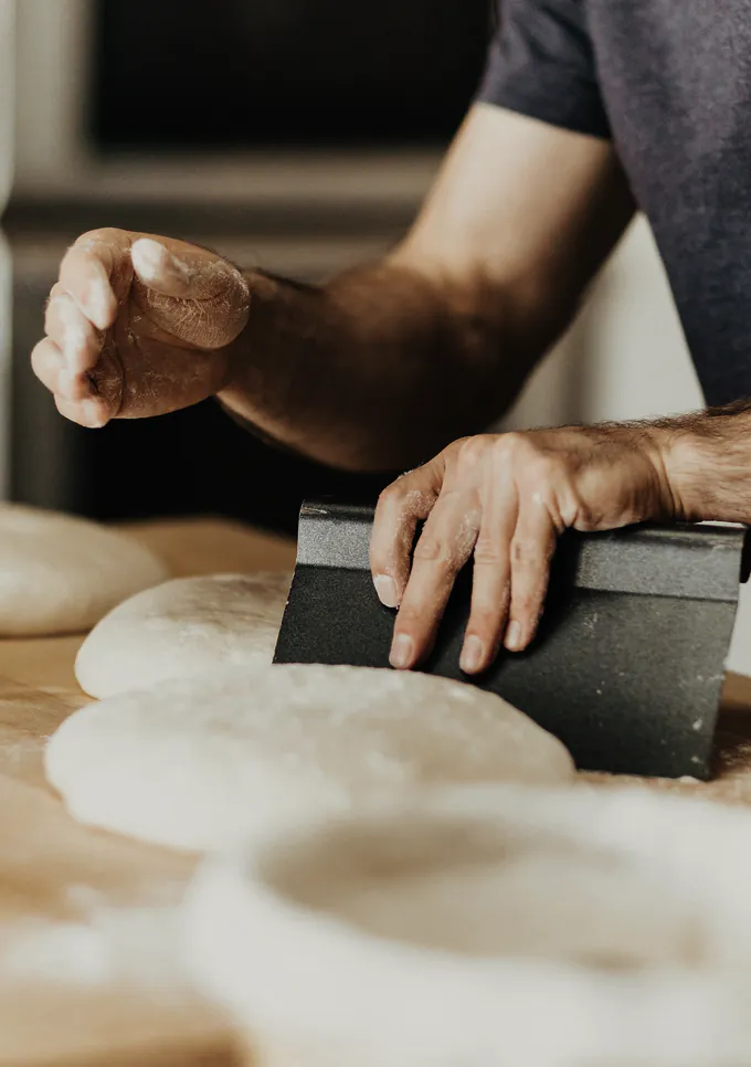 Forearms dividing dough with a bench scraper on a floured board